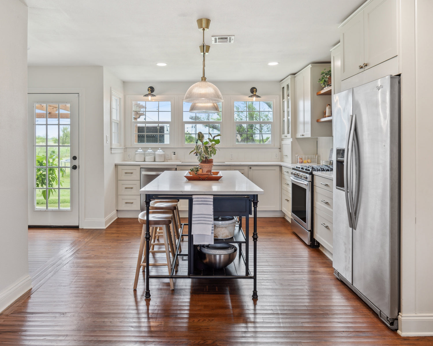 Modern kitchen with stainless steel appliances, wooden floor, and white cabinets.