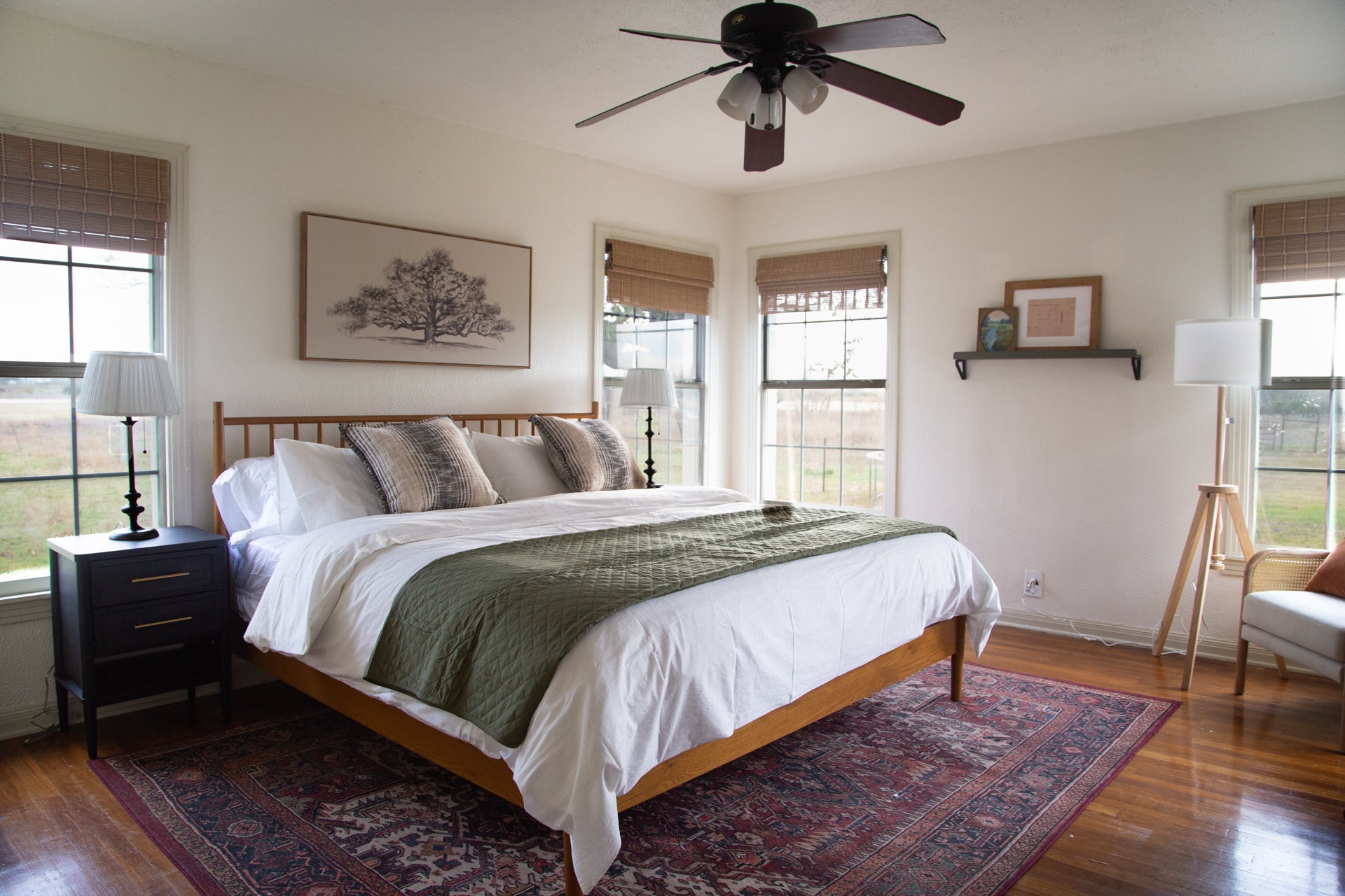 Primary bedroom with wooden king bed, green blanket, and large windows.